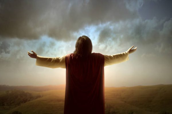 Rear view of Jesus Christ raised hands and praying to god with a sunrise sky background